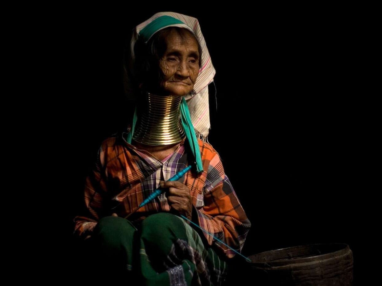 A woman of the Padaung (long neck) tribe sits contemplatively in her home.