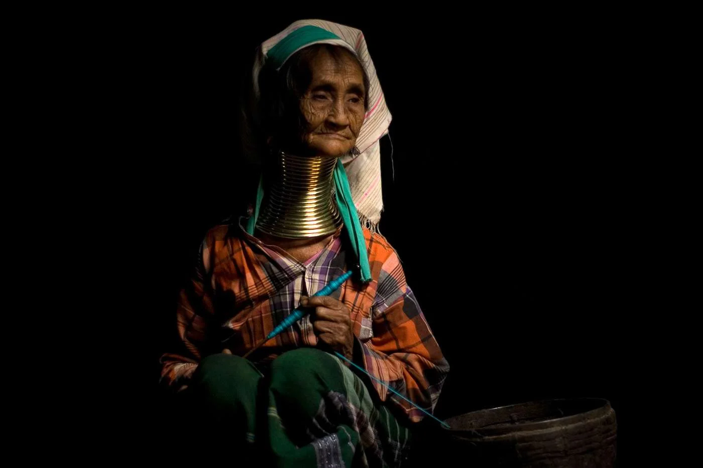 A woman of the Padaung (long neck) tribe sits contemplatively in her home.