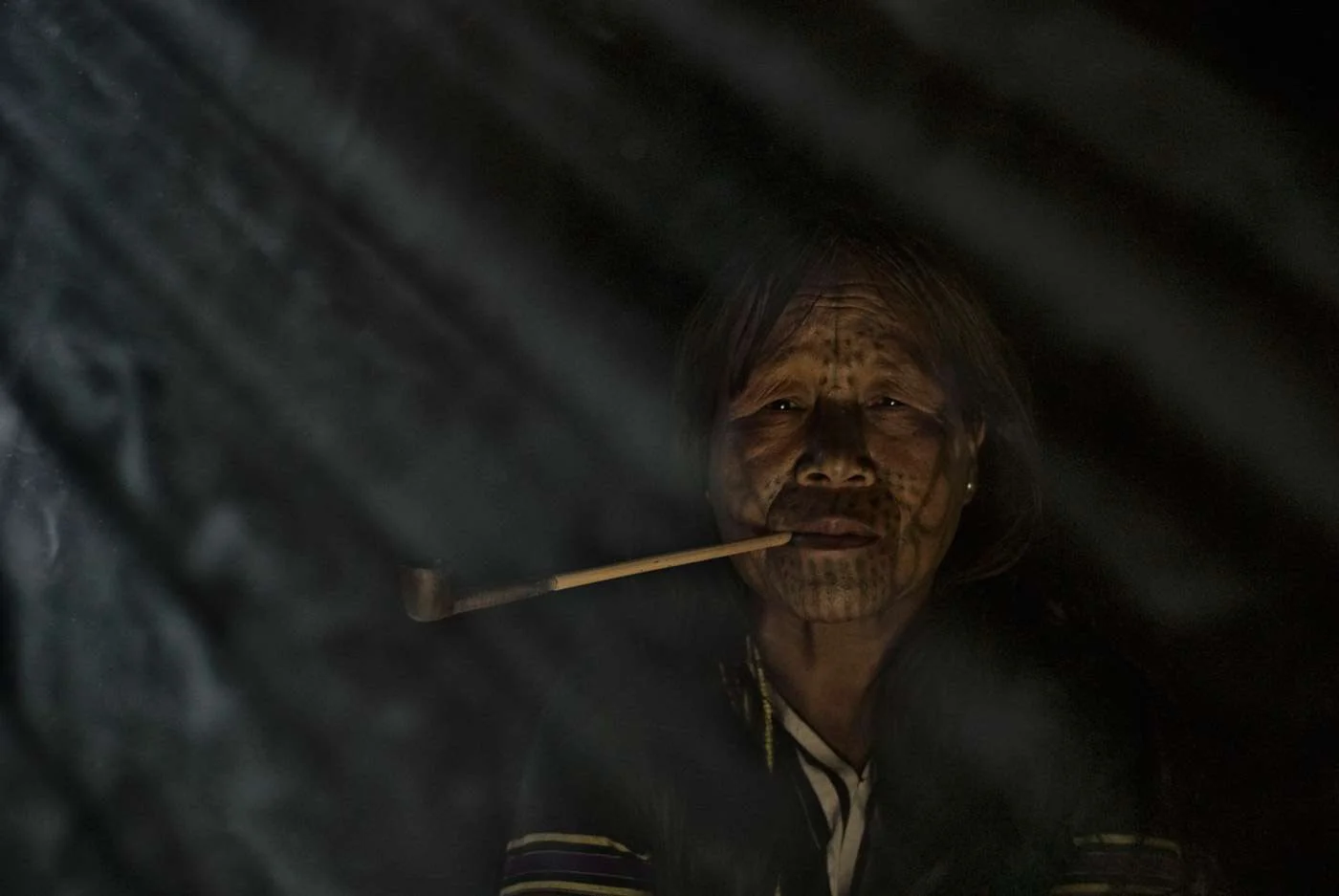 A tattoed Burmese lady enjoys a smoke in a remote village.